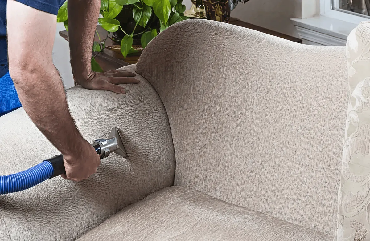 Professional upholstery cleaner deep-cleaning a fabric sofa with a handheld extraction tool and hose, Columbus, OH.